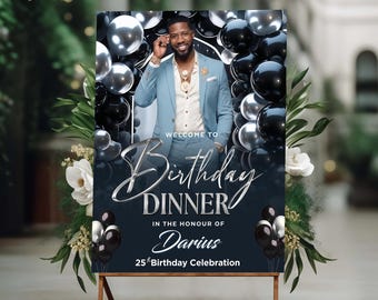 Puede incluir: Un letrero rectangular para una cena de cumpleaños con la foto de una persona en traje azul claro, rodeada de globos negros y plateados. El texto dice: Welcome to Birthday DINNER in the honour of Darius 25th Birthday Celebration.