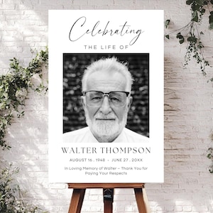 May include: A memorial sign on a wooden easel. The sign features a black and white portrait of a man with glasses, the text "Celebrating The Life Of" and the name "WALTER THOMPSON" with his birth and passing dates. The sign also includes the text "In Loving Memory of Walter - Thank You for Paying Your Respects."