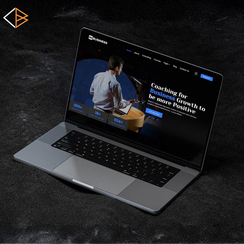 May include: A silver laptop showing a website with the text "INBUSINESS". The screen displays a man at a podium with the words "Coaching for Business Growth to be more Positive". The laptop is on a dark surface.
