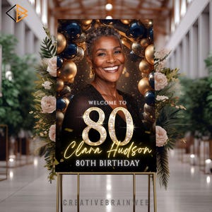 May include: A sign for an 80th birthday celebration. The sign features a smiling woman, gold and navy blue balloons, and floral arrangements. Text reads "Welcome to 80 Clara Hudson 80th Birthday."