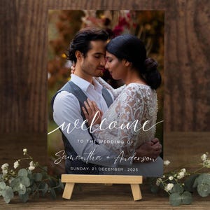 Pode incluir: Uma placa de boas-vindas de casamento em acrílico transparente com uma foto de um casal. A placa diz "welcome" em escrita cursiva, os nomes "Samantha + Anderson" e a data "SUNDAY. 21 DECEMBER. 2025". Apresentado em um pequeno cavalete de madeira.