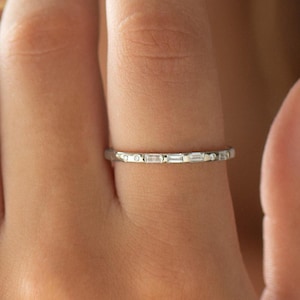 Op de afbeelding: Een delicate zilveren ring met een band van kleine, rechthoekige en ronde stenen. De ring wordt getoond op een vinger, waarbij het ingewikkelde ontwerp en de glans van de edelstenen worden benadrukt. Dit is een fijn sieraad.