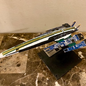 May include: A set of three ceramic mugs with a speckled, matte finish. The mugs are in shades of cream, light gray, and dark gray. Each mug has a simple, minimalist design and a rounded handle.