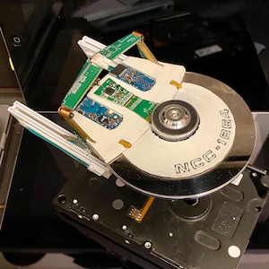 May include: A unique, handcrafted sculpture resembling a spaceship, constructed from computer components. The design incorporates a hard drive as the central body, with circuit boards and other electronic parts forming the ship's details. The text "NCC-1864" is visible.