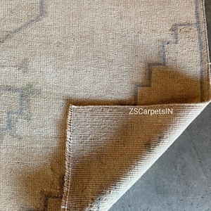 May include: Beige and grey rug with a geometric design. The rug has a textured surface and a folded corner, revealing the underside. The text "ZSCarpetsIN" is visible on the folded corner.