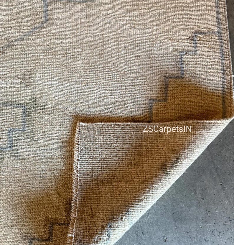 May include: Beige and grey rug with a geometric design. The rug has a textured surface and a folded corner, revealing the underside. The text "ZSCarpetsIN" is visible on the folded corner.
