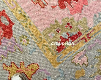 May include: Close-up of a colorful rug with a geometric pattern. The rug features a combination of pink, gray, yellow, and red hues. The design includes floral and cross-like shapes. The text "ZSCarpetsIN" is visible.