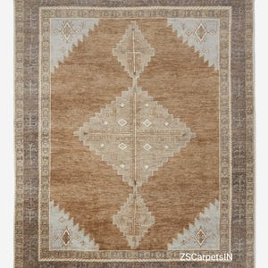 May include: A rectangular brown rug with a central diamond pattern in beige and light blue. The rug has a border with geometric designs and a textured appearance, suitable for home decor.