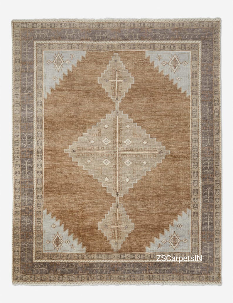 May include: A rectangular brown rug with a central diamond pattern in beige and light blue. The rug has a border with geometric designs and a textured appearance, suitable for home decor.
