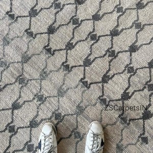 Puede incluir: Una alfombra tejida con una base de color beige claro y un patrón geométrico de rejilla repetitivo en gris oscuro. El diseño consiste en formas de diamante interconectadas con pequeños cuadrados de color gris oscuro en cada intersección. El texto ZSCarpetsIN es visible.