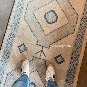 Könnte beinhalten: Beige und blau gemusterter Teppich mit geometrischen Mustern. Der Teppich hat ein zentrales Rautenmuster mit einem kreisförmigen Muster im Inneren, umgeben von blauen geometrischen Formen. Der Teppich hat ein strukturiertes Aussehen und der Text "ZSCarpetsIN" ist sichtbar.