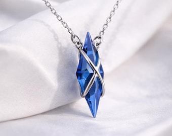 May include: A silver necklace featuring a faceted, blue crystal pendant. The crystal is diamond-shaped and encased in a silver metal frame. The pendant hangs from a delicate silver chain, creating a simple yet elegant design.