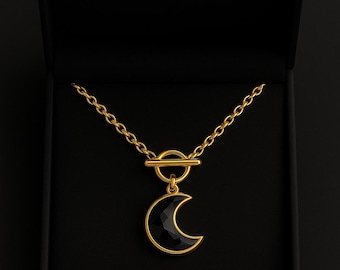 Puede incluir: Collar dorado con un colgante de media luna negra, presentado en una caja negra. El colgante de luna es facetado. La cadena tiene un diseño de eslabones delicados. Es una joya.