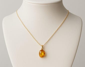 Könnte beinhalten: Eine goldfarbene Halskette mit einem Anhänger, der einen ovalen, bernsteinfarbenen Edelstein zeigt. Der Anhänger hängt an einer zarten Kette. Die Halskette wird auf einer weißen Schaufensterpuppe präsentiert.