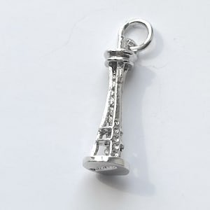 Könnte beinhalten: Silberner Anhänger in Form des Space Needle, einem berühmten Wahrzeichen von Seattle, Washington.