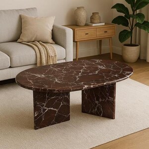 Op de afbeelding: Ovale salontafel met een donkerbruin marmeren blad en twee rechthoekige steunen. Het marmer heeft witte adering. De tafel heeft een modern design en staat op een lichtgekleurd tapijt.