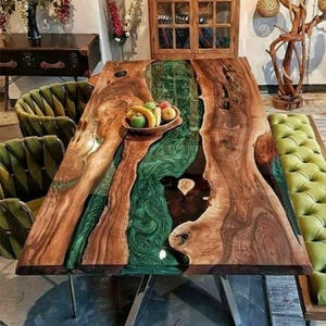 May include: A handcrafted wooden dining table with a river of green epoxy resin running through the center. The table features a natural wood grain finish and sits on metal legs. A bowl of fruit rests on the table's surface.