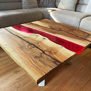 May include: A handcrafted wooden coffee table with a vibrant red resin river. The table features a natural wood grain pattern and is supported by silver metal legs. The table measures approximately 40 inches long and 20 inches wide.