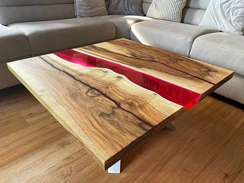 May include: A handcrafted wooden coffee table with a vibrant red resin river. The table features a natural wood grain pattern and is supported by silver metal legs. The table measures approximately 40 inches long and 20 inches wide.