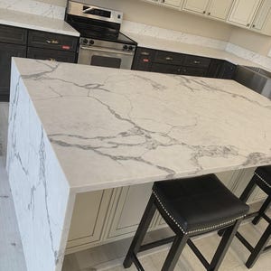 Pode incluir: Uma caneca de cerâmica branca com uma alça preta e o texto "But First, Coffee" em negrito preto. A caneca está sobre uma superfície de madeira. A caneca tem 10 cm de altura.