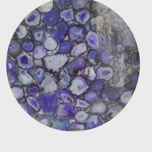 Può includere: Una lastra circolare caratterizzata da un mosaico di fette di agata lucida viola e bianca. La superficie mostra una disposizione densa di segmenti di pietra irregolari, dai toni viola e bianco traslucido, con venature naturali e strutture cristalline.