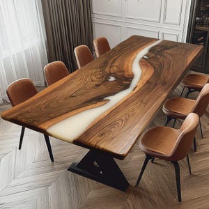 Puede incluir: Una gran mesa de comedor rectangular de madera con un río de resina blanca en el centro. Ocho sillas de cuero marrón rodean la mesa. La mesa tiene una base oscura y está sobre un suelo de madera clara. Dimensiones: aproximadamente 240 cm de largo.