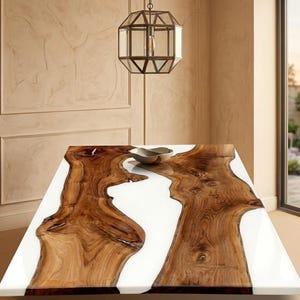 Peut inclure: Une table rectangulaire en bois avec un centre en résine époxy blanche. La table présente un design à bord vif avec un motif de grain de bois naturel. Un bol en métal est posé sur la table. Un luminaire décoratif suspendu est au-dessus de la table.