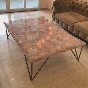 Peut inclure: Une table basse rectangulaire avec un plateau à motifs roses et blancs et des pieds en métal doré. La table est dans un salon avec un canapé.