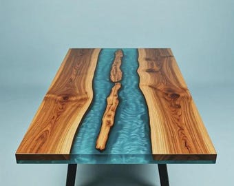 Può includere: Un tavolo rettangolare caratterizzato da due lastre di legno naturale con venature pronunciate, separate da un inserto centrale in resina turchese traslucida che imita un fiume. Il tavolo è sostenuto da gambe in metallo nero.