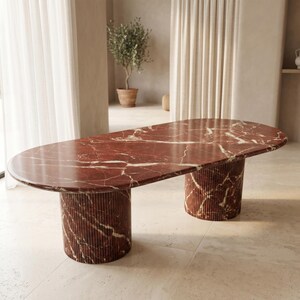 Puede incluir: Una gran mesa ovalada de mármol rojo con vetas blancas. La mesa tiene dos patas cilíndricas estriadas. La mesa es una pieza destacada para un comedor o sala de estar. La mesa mide aproximadamente 244 cm de largo.
