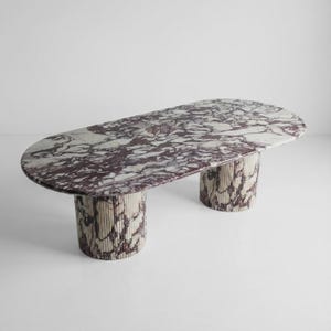 May include: An oval marble table with a white and burgundy pattern. The table has two cylindrical bases with a ribbed texture and matching marble design. A modern furniture piece.