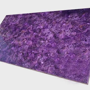 Può includere: Una lastra rettangolare di pietra ametista lucidata. La superficie mostra una ricca tonalità viola intenso con motivi intricati e variazioni di tono. La consistenza della pietra appare cristallina, con una finitura lucida. I bordi sono puliti e ben definiti.
