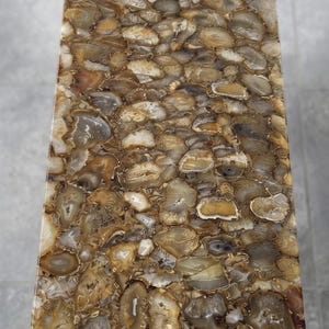May include: A rectangular table surface composed of numerous polished brown, tan, and translucent white agate slices embedded in a smooth resin finish. A small gold-toned metal sign with the text JimmysCraftStudio is placed at the top center.