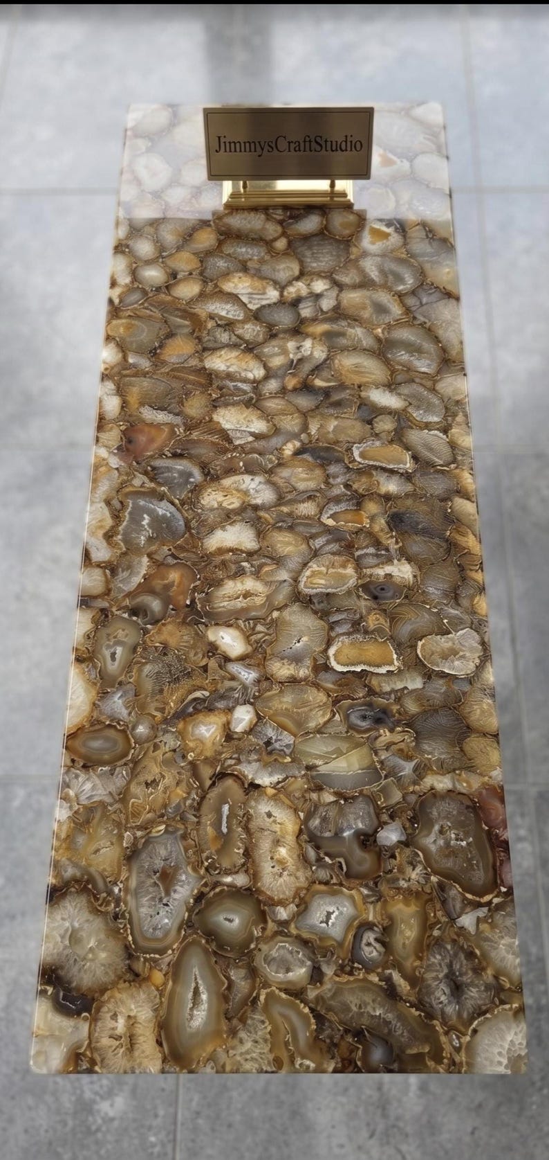 May include: A rectangular table surface composed of numerous polished brown, tan, and translucent white agate slices embedded in a smooth resin finish. A small gold-toned metal sign with the text JimmysCraftStudio is placed at the top center.