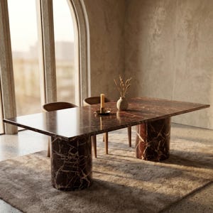 Op de afbeelding: Een rechthoekige eettafel met een donkerrode marmeren bovenkant en cilindrische marmeren poten. Een kaars, een kleine vaas met gedroogde planten en een kandelaar staan op de tafel. De tafel staat op een neutraal gekleurd tapijt.