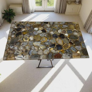 May include: A rectangular table featuring a mosaic surface composed of numerous polished agate slices in shades of gray, brown, gold, and white. The tabletop is supported by a dark metal base with thin, angled legs, viewed from a high angle.