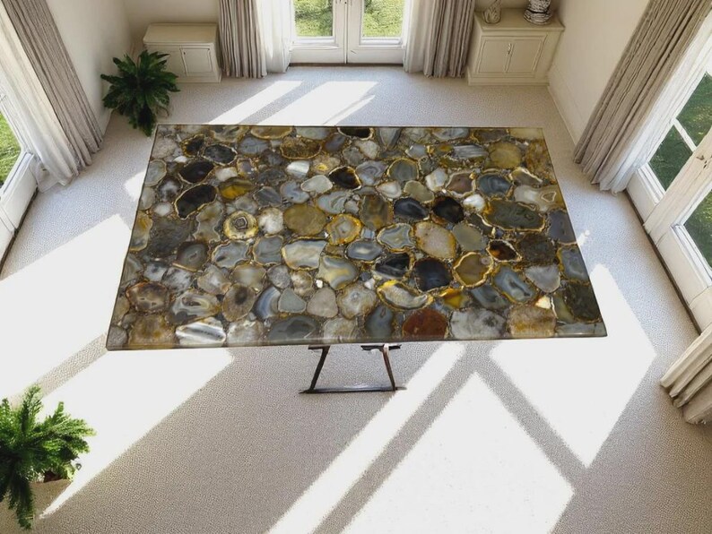 May include: A rectangular table featuring a mosaic surface composed of numerous polished agate slices in shades of gray, brown, gold, and white. The tabletop is supported by a dark metal base with thin, angled legs, viewed from a high angle.
