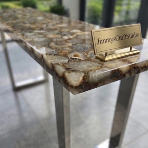 May include: A rectangular console table featuring a polished surface made of multi-tonal brown and cream agate slices. The table has a metallic silver frame and a small gold-toned rectangular plaque with the text JimmysCraftStudio.