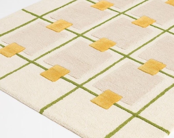 May include: A rectangular rug with a cream-colored background, featuring a grid pattern of green lines. Beige rectangles and yellow squares are evenly spaced throughout the design. The rug has a soft, textured appearance.