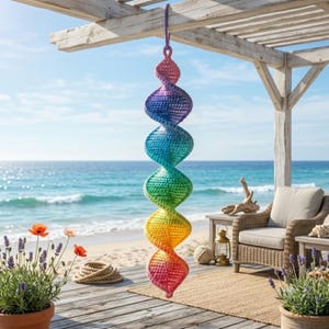 May include: A hanging crochet spiral ornament featuring a vibrant rainbow gradient of colors, transitioning from pink at the top to purple, blue, green, yellow, and orange, ending in a pink point, suspended by a matching purple yarn loop.