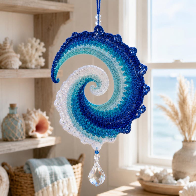 May include: A spiral-shaped crochet hanging ornament featuring a gradient of white, light blue, and dark blue yarn. The piece is suspended by a blue string with clear beads and features a faceted clear crystal drop at the bottom center.