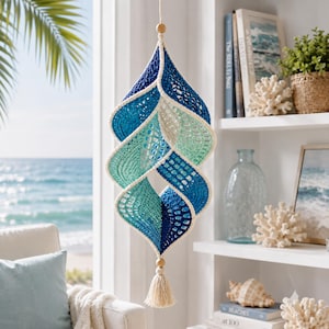 May include: A hanging spiral wind spinner crafted from crocheted yarn in gradient shades of dark blue, teal, and light green. The structure features an openwork pattern with a cream-coloured border, suspended by a string with wooden beads and a tassel.