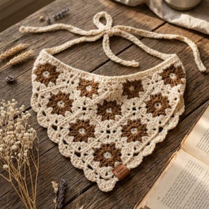 May include: A triangular crochet bandana featuring a repeating floral granny square pattern in cream and brown yarn. The accessory has a scalloped edge and long ties at the top corners for fastening. A small rectangular brown leather tag is attached.