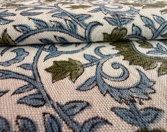 May include: Close-up of a folded fabric with a repeating floral pattern. The design features stylized leaves and vines in shades of blue and olive green against a cream-colored background. The fabric has a textured appearance.