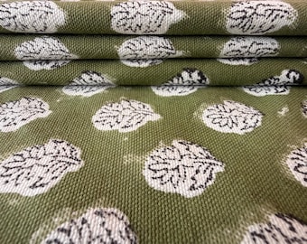 May include: A folded piece of olive green fabric featuring a repeating pattern of white and black leaf-shaped motifs. The textile has a visible woven texture with the leaves arranged in a consistent grid across the surface of the material.