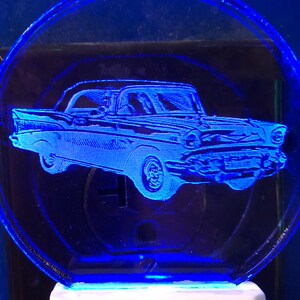 May include: A blue night light with a white base. The night light features a clear plastic cover with a silhouette of a classic car.