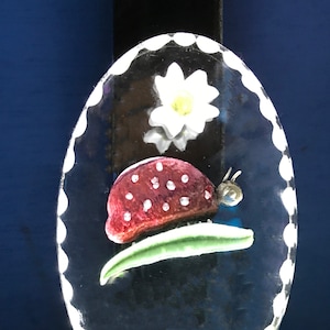 May include: A white night light with a clear glass dome featuring a red ladybug with black spots, a green leaf, and a white flower with a yellow center.