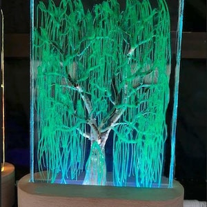 May include: A green willow tree sculpture encased in a clear acrylic block with a wooden base. The sculpture is illuminated from below with a warm white light.