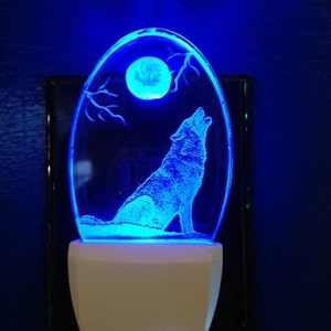 May include: A blue LED night light with a wolf howling at the moon design. The night light is oval shaped and has a white base.
