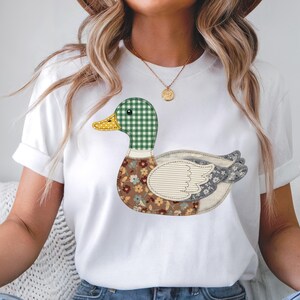 May include: White t-shirt featuring a colorful duck design. The duck has a green and white checkered head, a yellow beak, and a body with floral and patterned fabric details. The shirt is a casual, everyday wear item.
